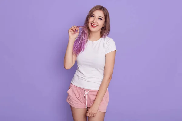 幸せな笑い若いです女の子で白いTシャツとローズ短い 見てカメラで浮気式 保つ指で彼女のライラック髪 ポーズ孤立した以上紫の背景 — ストック写真