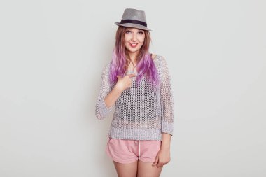 Şapkalı sevimli bir kadın kameraya bakıyor ve kendini işaret parmağıyla işaret ediyor. Gömlek ve şık bir şapka giyiyor. Onu seçen inanılmaz biri..