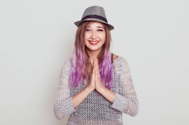 Mutlu pozitif kadın doğrudan kameraya bakıyor, avuç içlerini birbirine bastırıyor, birine dua ediyor, şükranlarını sunuyor, dişlek bir gülümsemesi var, beyaz arka planda izole edilmiş..