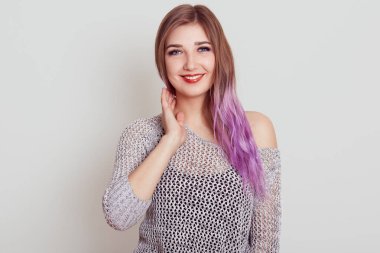 Hoş görünümlü, eflatun saçlı, kameraya gülümseyen, el ele gezen, gri gömlekli, gri arka planda soyutlanmış genç bir kadın..