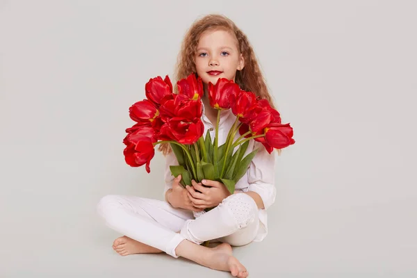 Blondynka Dziecko Siedzi Podłodze Skrzyżowanymi Nogami Trzymając Bukiet Czerwonymi Tulipanami — Zdjęcie stockowe