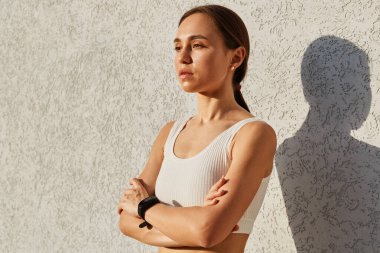 Beyaz bluz giyen, kendine güvenen ve kollarını kavuşturmuş düşünceli ve düşünceli bakışlarla yüzünü çeviren zayıf, çekici bir kadının yan görünüşü..