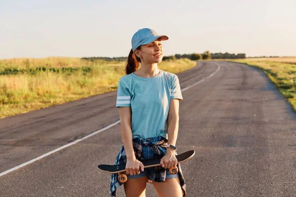Mooi Vrouwtje Met Blauw Shirt Vizierkap Met Skateboard Handen Wegkijkend — Stockfoto