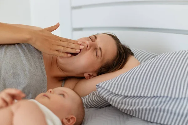 Retrato Interno Mãe Cansada Deitada Cama Com Bebê Menino Bocejando — Fotografia de Stock