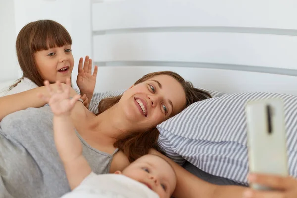 Happy Positive Female Lying Bed Her Children Holding Smart Phone — Stock Photo, Image