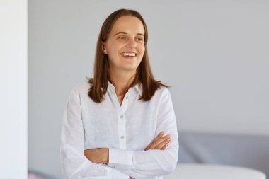 Kapalı alanda gülümseyen mutlu bir kadının kollarını kavuşturup olumlu ifadelerle, kendinden emin ve iyimser bir şekilde bakışlarını çevirdiği portresi..