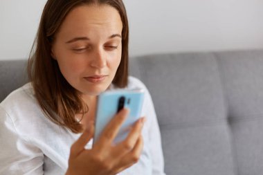 Beyaz gömlekli hasta bir kadının yakından çekilmiş portresi akıllı telefon ekranına yakından bakıyor, gözlerle ilgili sorunları var, cep telefonu ekranında ne gösterdiğini göremiyor,.