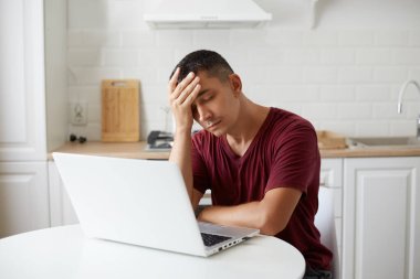 Kestane rengi bir tişört giyen yorgun bir adamın portresi mutfak takımının karşısında oturuyor, gözlerini kapatıyor, baş ağrısı çekiyor, uzun saatler çalışıyor, bitkin düşüyor..