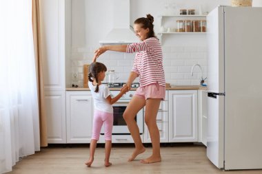 Mutlu, iyimser anne ve kızın uzun bir portresi evde mutfak setinin karşısında dans ediyor, günlük giyiniyor, mutluluğu ifade ediyor, çocukluğu anlatıyor..