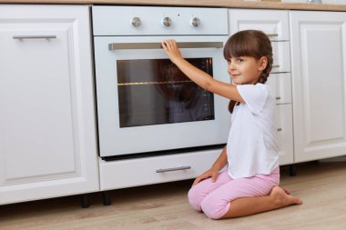Koyu renk saçlı kadın çocuk portresi mutfak setinin yanında oturmuş, başka tarafa bakıyor, lezzetli hamur işlerini bekliyor, günlük kıyafetlerini giyiyor..