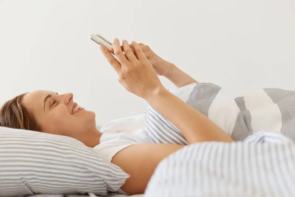Yatakta Battaniyenin Altına Uzanmış Akıllı Telefon Kullanan Mutlu Mutlu Bir — Stok fotoğraf