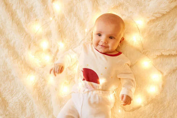 かわいい女の子は明るいクリスマスの庭の近くの柔らかいカーペットの上に床に横たわって 魅力的な笑顔で見上げ 白いお祝いの服を着て — ストック写真