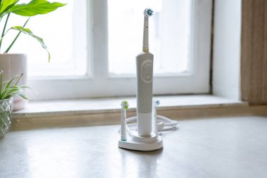 Elektrikli bir diş fırçası, küçük bir fabrikanın yanındaki şarj aletinin üzerinde duruyor. Temiz bir tezgah ve camdan gelen doğal ışığı gösteriyor..