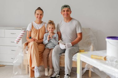 Gülümseyen aile oturmuş, resim yapmaya hazır. Ebeveynler ve şirin kızlar ev yenileme projeleri sırasında DIY araçlarıyla poz veriyorlar.