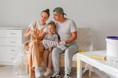 Aile resim yaparken mola veriyor. Anne, telefona ve gülümseyen kızına bakar..