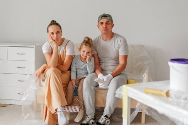 Yorgun aile bireyleri, evlerini geliştirme çabalarının ortasında bir koltuğa oturup birlikte yaşadıkları yeri boyarken bir süre dinleniyorlar..