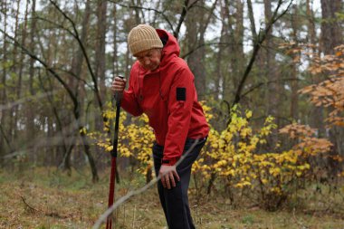 Kırmızı ceketli ve şapkalı bir adam ormanda yürüyüş yapıyor. Bir baston kullanır ve etrafındaki güzel sonbahar yapraklarına hayran kalır..