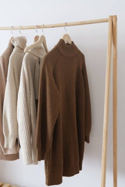 Tarafsız renklerde, yumuşak, sıcak süveterler ahşap bir askıda asılı, minimalist bir ortamda şık sonbahar moda fikirleri sunuyor..