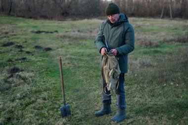 Sakin bir çim tarlasında, bir adam dışarıda maceraya hazır bir şekilde gün batımında teçhizatını hazırlıyor. Elinde ekipman, odaklanmış gözler var..