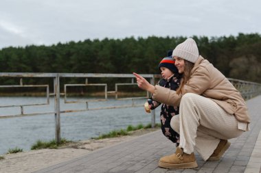 Bir kadın ve küçük çocuğu nehrin kenarında çömelmiş doğanın tadını çıkarıyor ve gördükleri bir şeyi işaret ediyorlar. Çevrelerinde mutlu ve meşgul görünüyorlar..