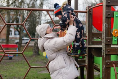 Bir kadın çocuğunu çocuk parkında kaldırır. Gülümsüyorlar ve birlikte vakit geçiriyorlar. Öğleden sonra güneş üzerlerine doğuyor..