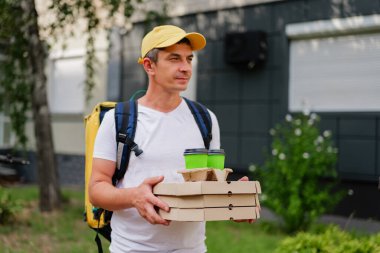 Teslimatçı bir binanın yakınındaki açık alanda birkaç pizza kutusu ve içecek tutuyor. Sahne, gün boyunca tipik bir doğum anını gösteriyor..