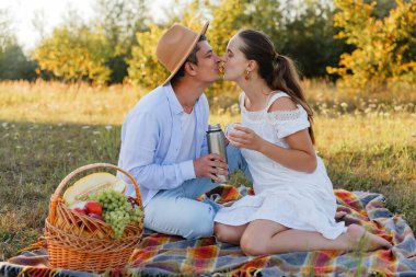 Çimenli bir tarlada battaniyeye iki kişi oturur. İçkinin ve meyve sepetinin tadını çıkarırken öpüşürler. Sıcak öğleden sonra ışığı altında ağaçlar etraflarını sarar..