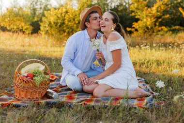 İki kişi bir tarlada battaniyede birlikte oturur. Sıcak bir öğleden sonra güneşinde sepetten gelen yemeğin tadını çıkarırken gülümser ve bir anı paylaşırlar..