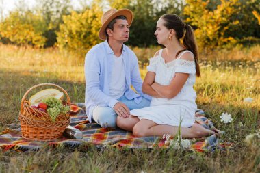 Bir çift piknik yaparken bir tarlada battaniyeye oturur. Yumuşakça konuşurlar ve doğada güneşli bir öğleden sonra meyve sepetinin tadını çıkarırlar..