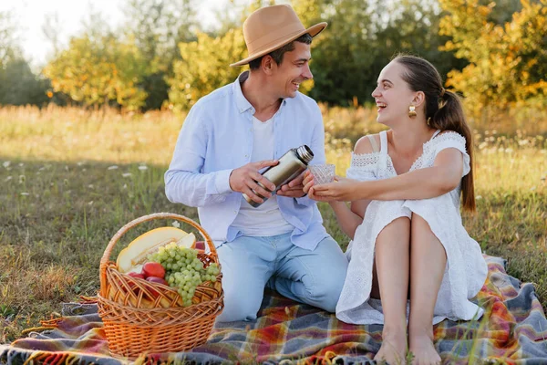 Güneşli bir tarlada ağaçlarla çevrili bir piknik sırasında iki kişi içki ve kahkaha paylaşıyor. Bir sepet meyveyle battaniyeye otururlar..