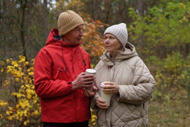 İki yaşlı birey ormanda birbirlerine yakın dururlar. Kahve fincanlarını tutarlar ve ağaçların arasında konuşurlar ve hava için sıcak giyinmiş yapraklar dökerler..