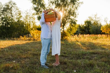 Bir çift gün batımında çimenli bir tarlada duruyor, birlikte sepet kaldırıyorlar. Güneş arkalarında parlıyor, sahnede sıcak bir ışık yaratıyor..