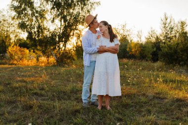 Bir erkek ve bir kadın gün batımında bir tarlada hassas bir anı paylaşıyorlar. Doğayla çevrelenmiş bir şekilde, güneş sıcacık bir parıltı saçar..