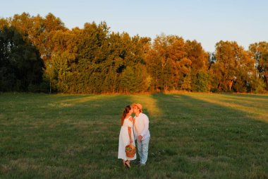 Çimenli bir alanda el ele tutuşup öpüşen iki insan. Gün batımında güneş onların üzerine doğuyor..