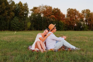 Çimenli bir tarlada battaniyeye uzanmış bir çift rahatlıyor. Güneş ağaçların arkasında batarken sıcak ve samimi bir manzara yaratarak bir anı paylaşıyorlar..