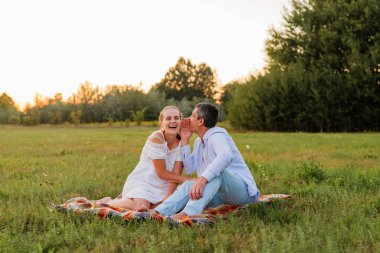 Akşam saatlerinde bir tarlada battaniyede iki kişi birlikte oturur. Sıcak havanın ve doğanın tadını çıkarırken gülücüklerini ve kahkahalarını paylaşıyorlar..
