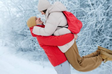 Bir çift karda oynar, adam kadını yüzlerinde gülümsemeyle havaya kaldırır. Beyaz ağaçlarla çevrili ve soğuk bir kış manzarası var..