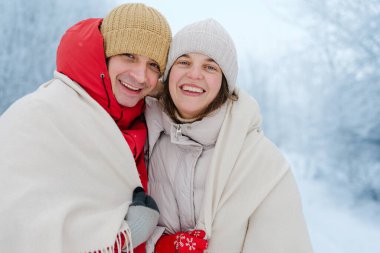 İki insan, ormanda karlı bir öğleden sonra sıcak battaniyelere sarılmışken gülümser. Soğuk hava için giyinmişler ve birlikte mutlular..