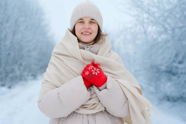 Sıcak giysiler içinde karlı bir arazide duran bir kadın. Hafif bir atkısı var ve ellerini birarada tutuyor, kırmızı eldivenlerini gösteriyor..