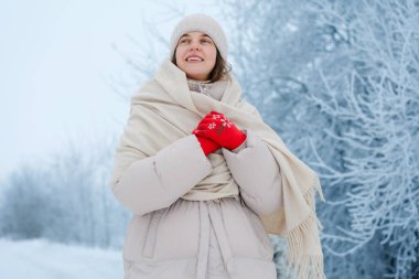 Sıcak bir palto ve kırmızı eldivenler giyerken, etrafı don kaplı ağaçlarla çevrili, karlı bir tarlada duran bir kadın. Açık gökyüzünün olduğu bir kış günü..