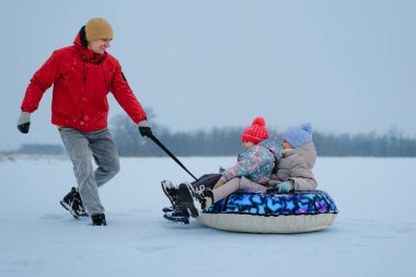 Bir adam kışın karlı bir arazide kızakla iki çocuk çekiyor. Soğuk havada eğlenirken kar nazikçe düşüyor..