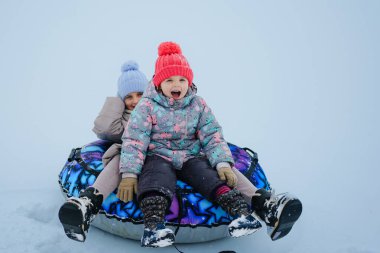 Karlı bir yamaçtan aşağı kayarken gülümseyen ve gülen iki çocuk. Sıcak kıyafetler giyerler ve soğuk bir günde kış etkinliğinin tadını çıkarırlar..