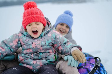 İki çocuk karlı bir tepeden kayıyor. Bir çocuk kahkaha atarken diğeri neşeyle bağırıyor. İkisi de renkli kışlık şapkalar ve kalın elbiseler giyiyor..