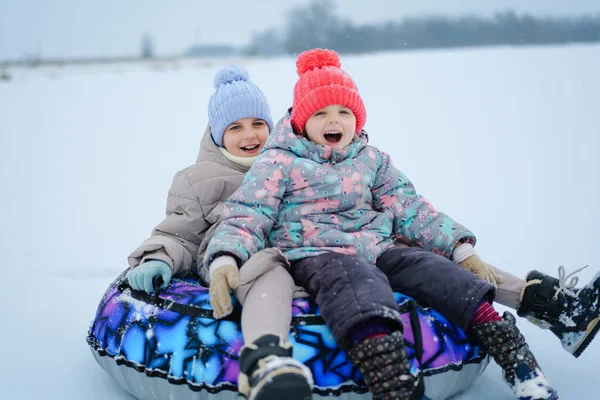 Çocuklar karlı bir tarlada bir kar tüpünde birlikte otururlar. Soğuk havada eğlenceli bir anı paylaşırken gülümser ve kalın elbiseler giyerler..
