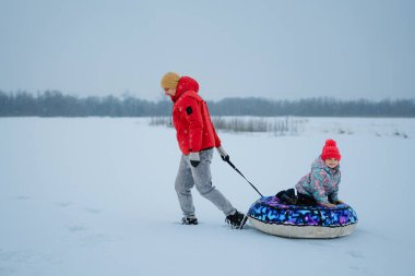Bir adam, genç bir kızı kışın karlı bir tarlada kar borusuna çekiyor. Soğuk bir ortamda yağan karla birlikte açık havada eğleniyorlar..