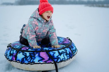 Bir çocuk metroyla karlı bir tepeden kayıyor, kış gününde heyecan gösteriyor. Kar zemini kaplıyor ve çocuk parlak bir palto ve şapka giyiyor..