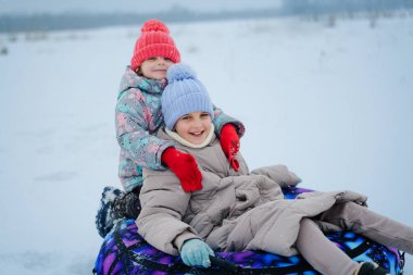 İki çocuk, serin bir parkta sıcak şapkalar ve eldivenlerle karlı bir tepeden aşağı kayarak gülüyor ve birlikte eğleniyorlardı..