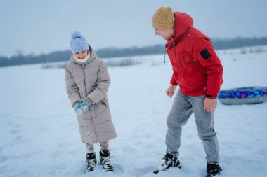 İki çocuk karda eğleniyor. Bir çocuk ceket ve eldiven giyerken diğeri gülüyor. Soğuk bir günde donmuş bir gölün yanında oynarlar..