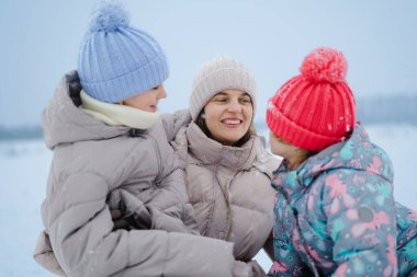 Çocuklar ve yetişkinler dışarıda karda neşeli bir anı paylaşıyorlar. Onlar kalın giysiler ve renkli şapkalar giyerler. Etraflarına hafifçe kar yağar.