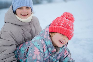 Çocuklar karlı havada dışarıda vakit geçirmeyi severler. Kış için sıcacık giyinip gülüp oynuyorlar. Kar taneleri renkli kış kıyafetlerini örtüyor..
